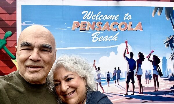 Steve and I, with my head on his shoulder, are standing in front of a sign that says Welcome to Pensacola Beach.