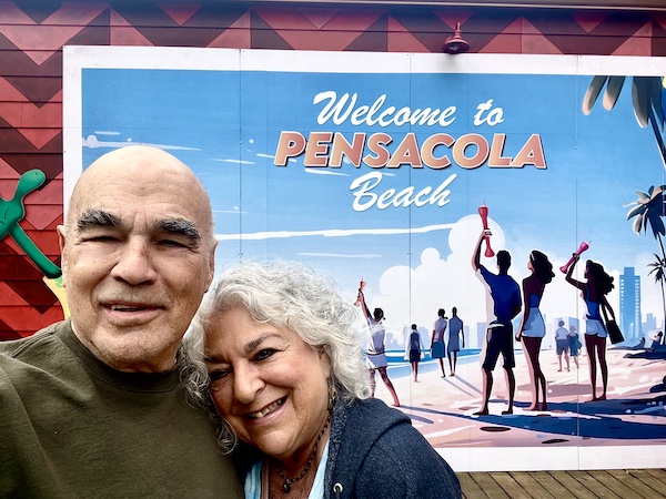 Steve and I, with my head on his shoulder, are standing in front of a sign that says Welcome to Pensacola Beach.