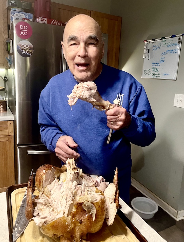 Steve, in a blue sweatshirt, about to take a bite from our Thanksgiving turkey leg.