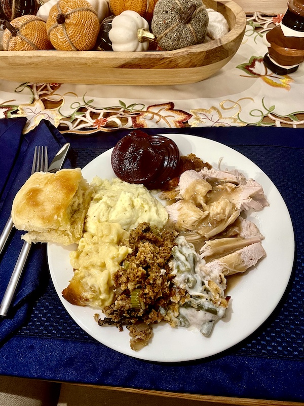 White dinner plate topped with sliced turkey, gravy, stuffing, mac and cheese, mashed potatoes, green bean casserole, rolls and cranberry sauce for our Thanksgiving in March?