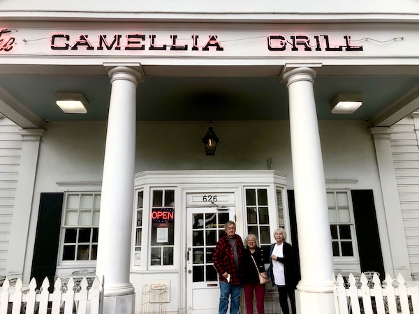 Two women with silver hair and a man in a red plaid shirt on the steps at the entrance to Camellia Grill New Orleans