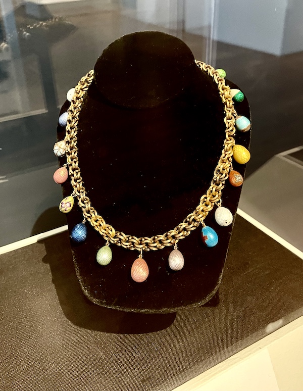Gold chain necklace with colorful tiny Easter eggs hanging from the chain on a black velvet display at the New Orleans Museum of Art