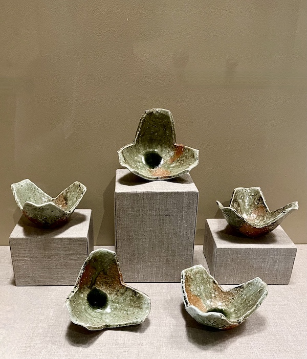 Moss green and orange pottery plates in the shape of split peppercorns on display at the New Orleans Museum of Art