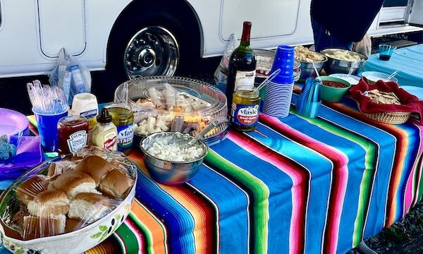 Brightly colored Mexican blanket covers a buffet table topped with all of the fixings for sandwiches. Also there is a charcuterie board and bottles of wine