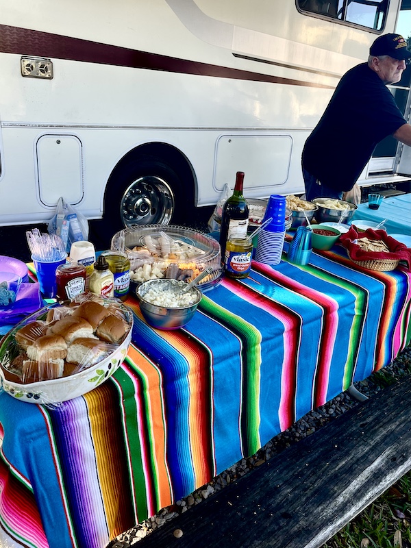Brightly colored Mexican blanket covers a buffet table topped with all of the fixings for sandwiches. Also there is a charcuterie board and bottles of wine