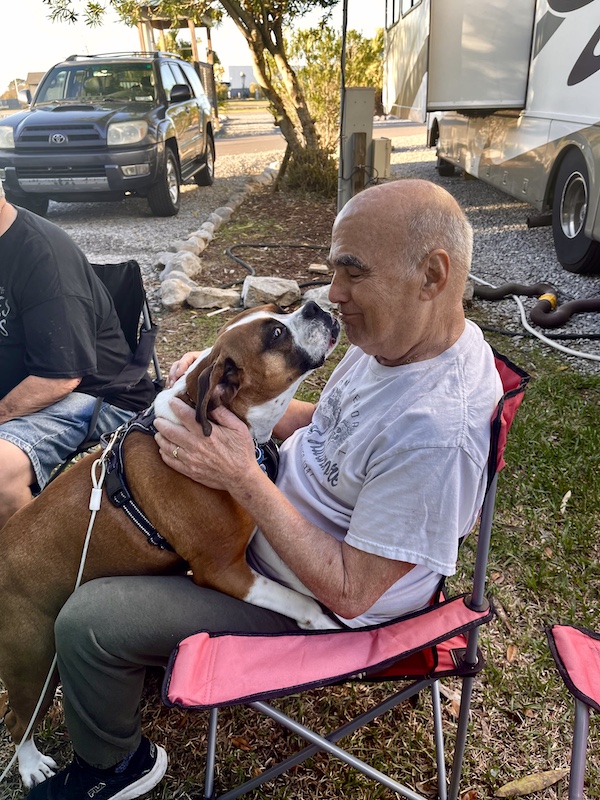Steve sitting in a red camping chair with beautiful boxer giving him a kiss at New Orleans RV Resort and Marina