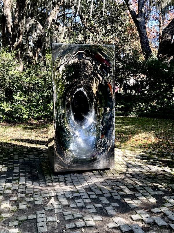 Rectangular shiny steel sculpture on gray pavers under hanging Spanish Moss. Photo taken while Sharing Sculpture Garden with Friends