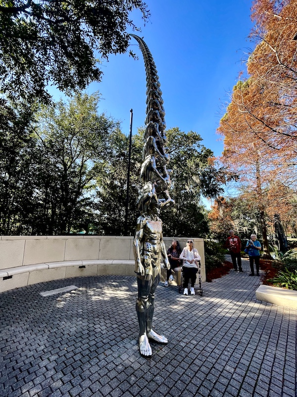 Extremely tall statue of a man with successive men stand on his shoulders. Each man is smaller than the one before as it soars to the sky. Photo taken while Sharing Sculpture Garden with Friends