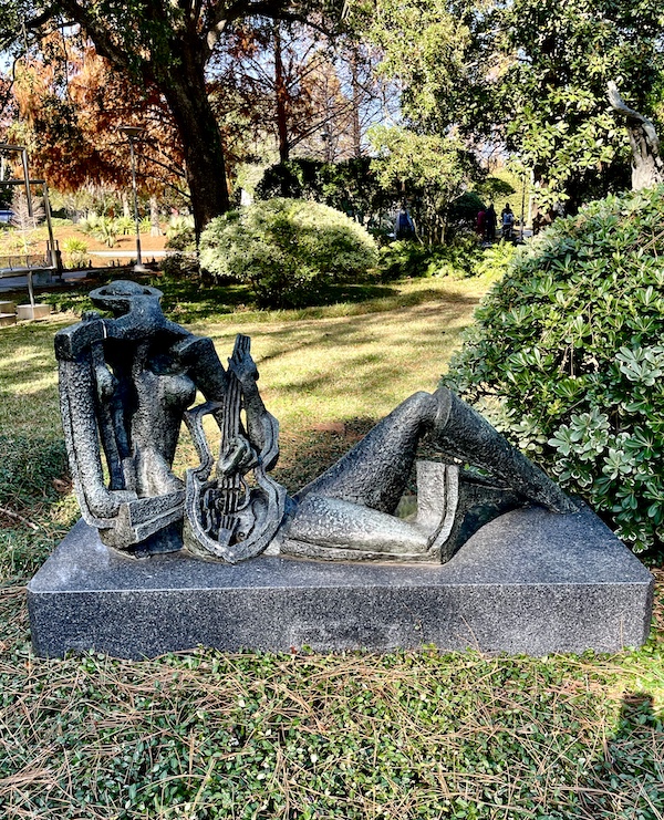 Stylized sculpture of a person with a violin sitting on the ground seen while Sharing Sculpture Garden with Friends