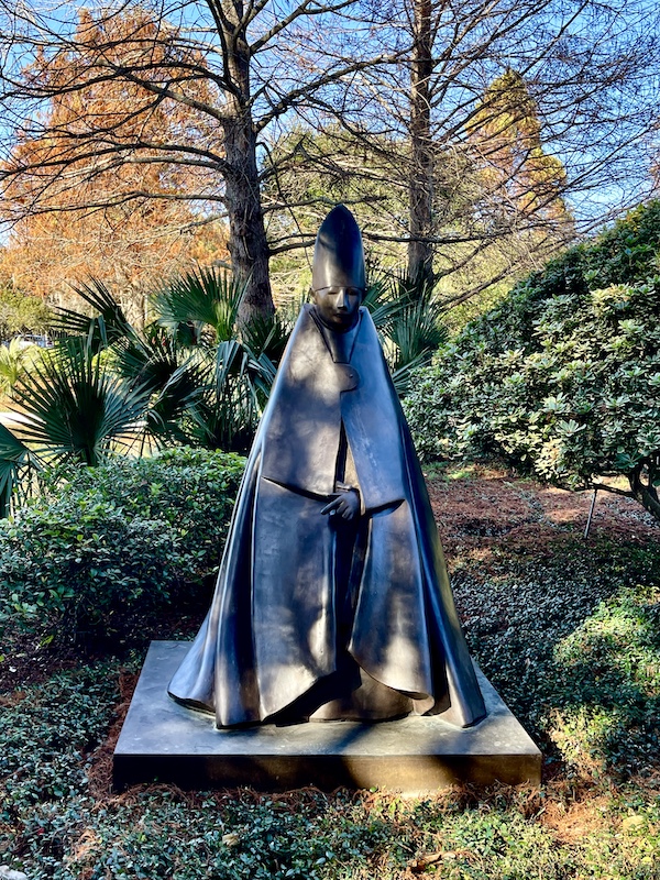 Bronze of a Cardinal in robes with mitre on his head seen while Sharing Sculpture Garden with Friends