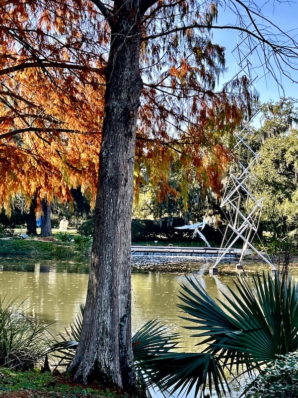 Sculpture of metal origami birds coming out of the water, seen through the trees while Sharing Sculpture Garden with Friends