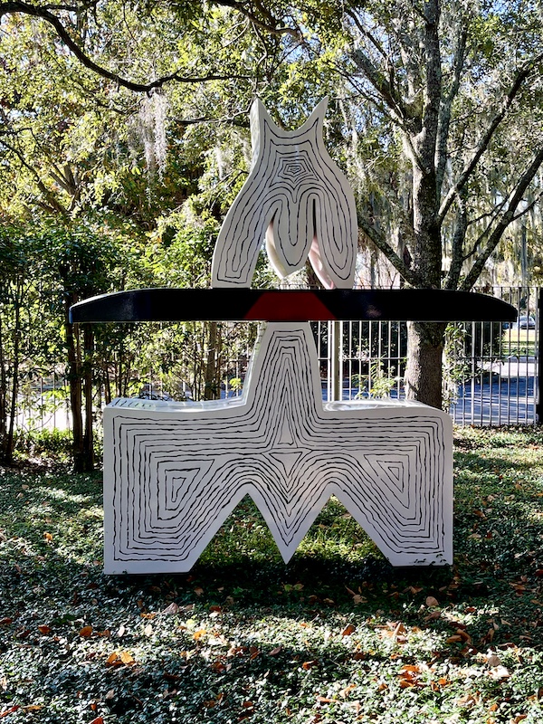 Modern sculpture in white with black lines and color in the shade of the gardens.