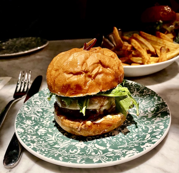 Thick cheeseburger with brioche bun on green and white plate at The Columns New Orleans