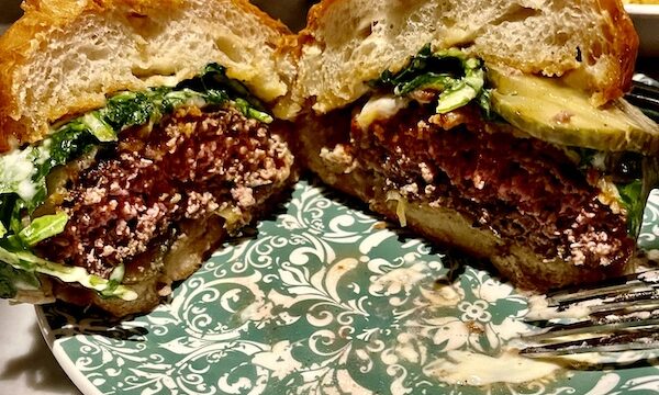 Perfectly cooked hamburger on brioche bun with lettuce, melted cheese and sauce, cut in half on green and white plate at The Columns New Orleans