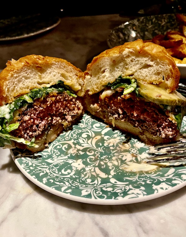 Perfectly cooked hamburger on brioche bun with lettuce, melted cheese and sauce, cut in half on green and white plate at The Columns New Orleans