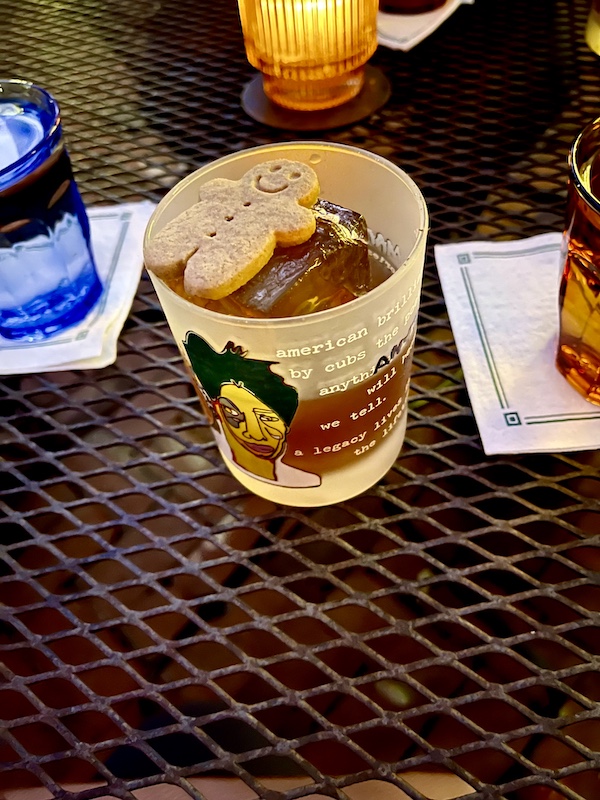 Hand painted rocks glass filled with a cocktail, large artisanal ice cube with gingerbread man cookie floating on top at The Columns New Orleans