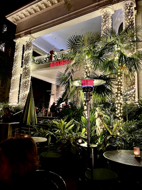 Tropical landscape and torch heater with strings of twinkle lights on the white columns of the covered patio at The Columns New Orleans