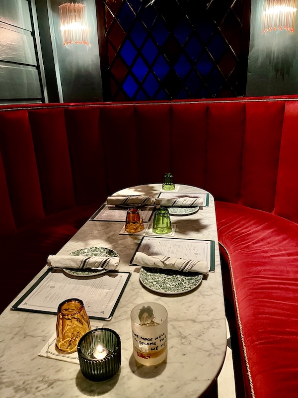 Large booth with red velvet upholstery and long table set with green and white print china, cloth napkins and glassware at The Columns New Orleans