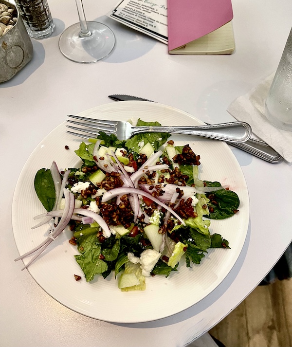 White plate topped with salad greens, strawberries, pecans and crumbled feta with red onion slivers at The Vault Tulsa Oklahoma