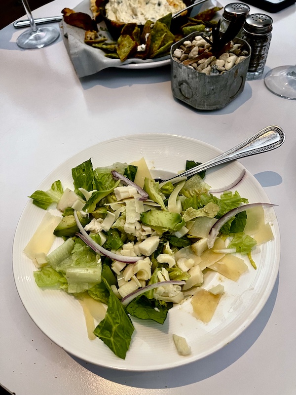 White plate topped with salad greens, avocado, red onion slivers and shaved parmesan cheese at The Vault Tulsa Oklahoma