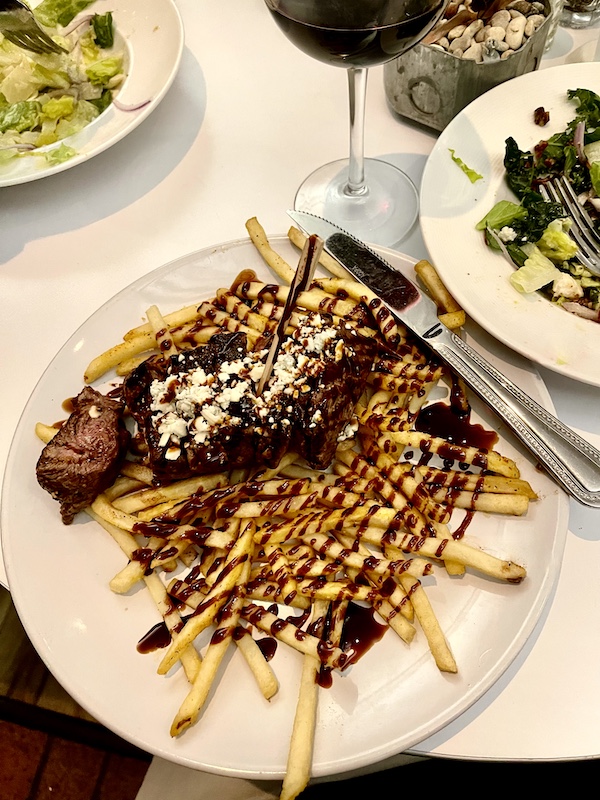 White plate topped with sliced steak, blue cheese crumbles, French Fries and drizzled with balsamic glaze at The Vault Tulsa Oklahoma