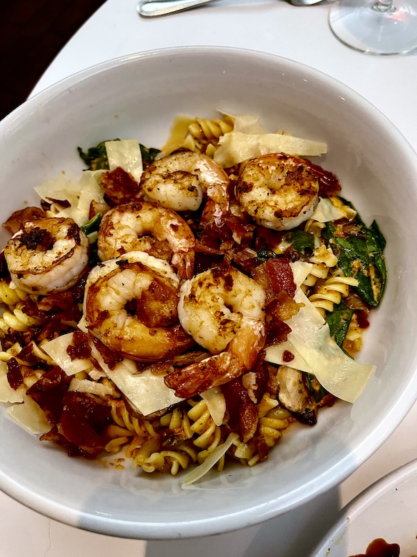 Deep white bowl filled with rotini pasta, grilled shrimp, spinach, shaved Parmesan and sun-dried tomato cream sauce at The Vault Tulsa Oklahoma