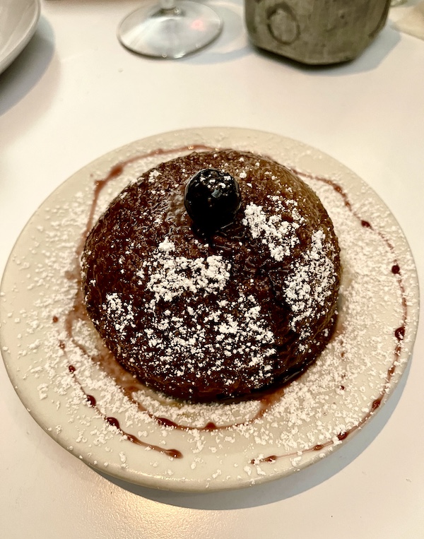 Cream colored plate topped with a domed individual cake covered in powder sugar with decorative drizzle on plate at The Vault Tulsa Oklahoma