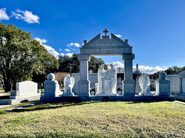 White marble statues and ornate arch on the lawn at the Private Estate area of Historic Metairie Cemetery Louisiana