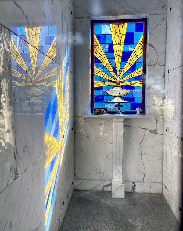 Eternal flame stained glass window shows a lamp, flame, yellow light rays and blue background at the Historic Metairie Cemetery Louisiana