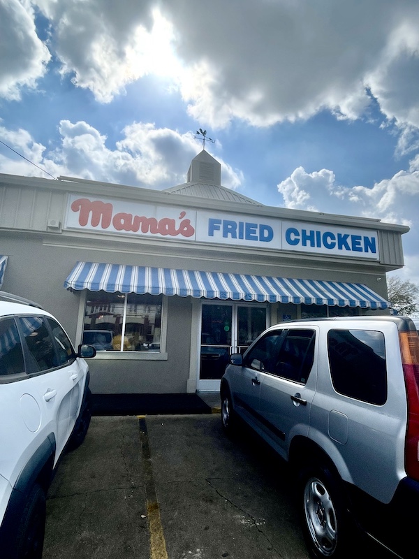 Small stand alone restaurant, Mama's Fried Chicken Opelousas LA, has a striped awning and lit sign out front.