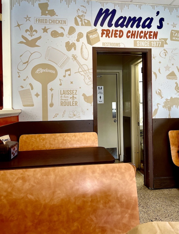 Inside Mama's Fried Chicken Opelousas LA with wooden booths and cute wallpaper in dining area.