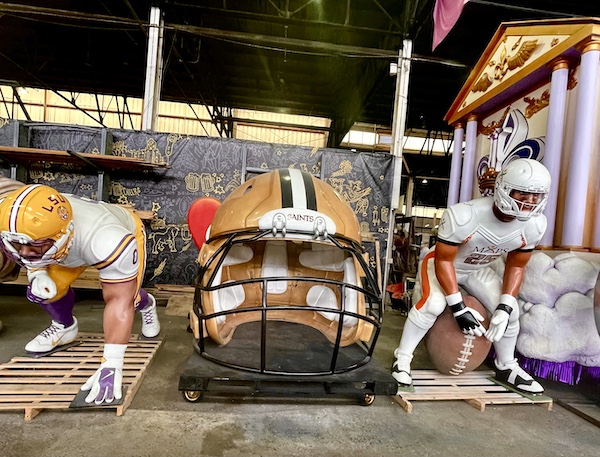 Two football player sculptures and a giant New Orleans Saints football helmet at Mardi Gras World NOLA