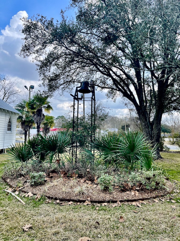 Bell atop a black frame in a garden at Le Vieux Village Opelousas LA