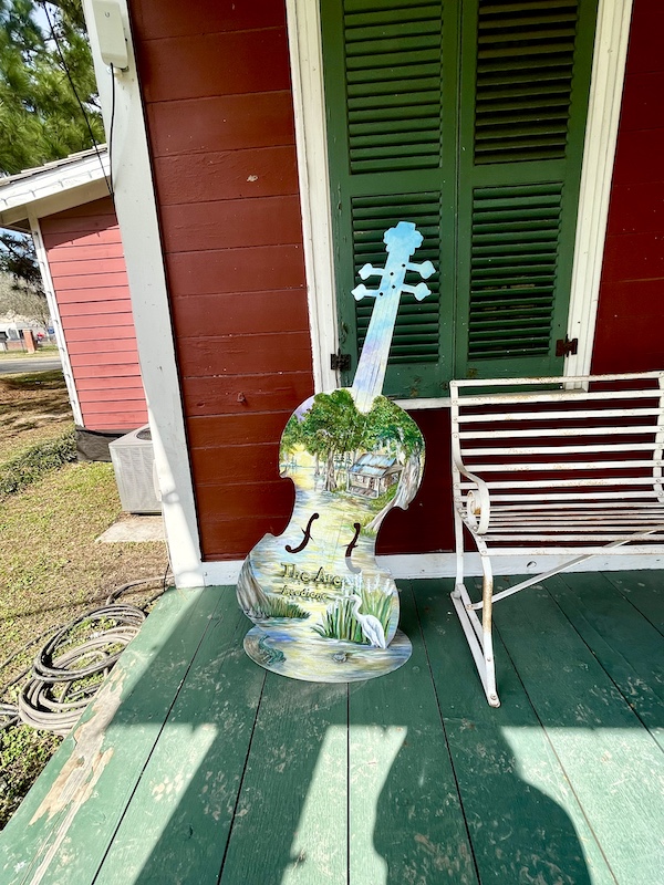Artfully painted guitar leans on red house with green wood porch floor in Le Vieux Village Opelousas LA