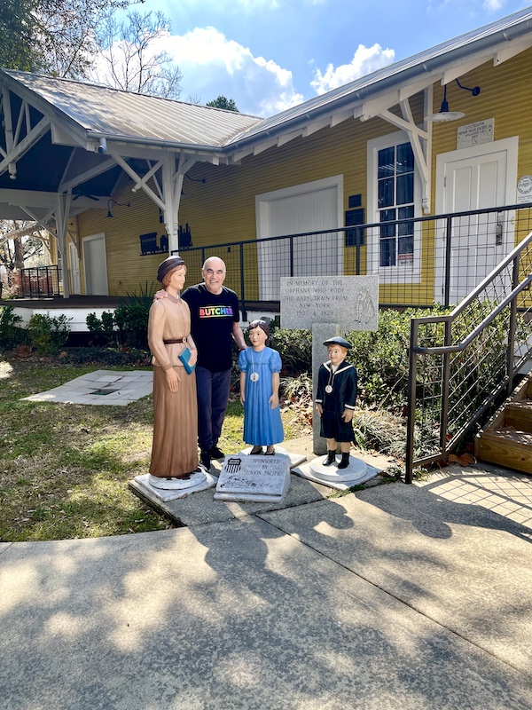 Steve standing among statues of a woman and two children in front of a building in Le Vieux Village Opelousas LA