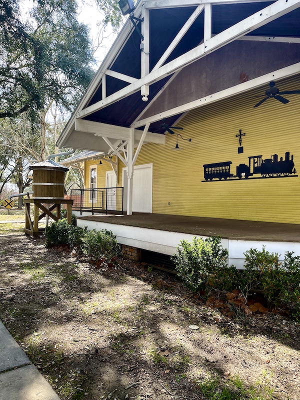 Yellow clapboard building with black train decor on side at Le Vieux Village Opelousas LA