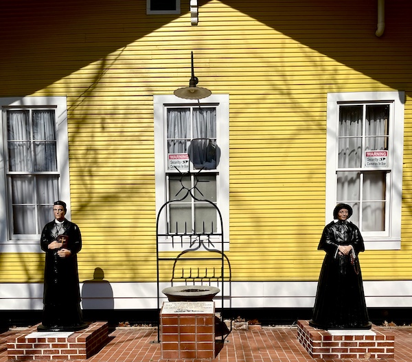 Yellow building with statues of a priest and nun in front at Le Vieux Village Opelousas LA