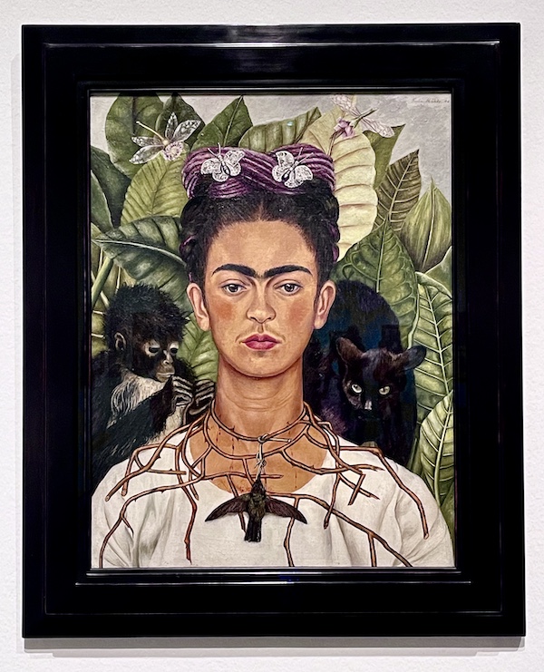 Painting of Frida with small monkey, thorn necklace, black cat and hummingbird on display at the Frida Kahlo Exhibit Houston