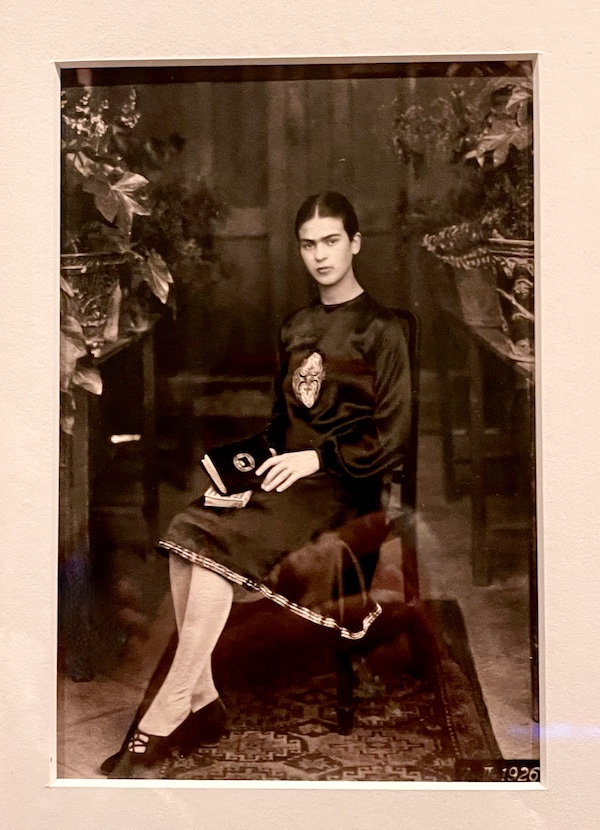 Sepia toned photo of artist Frida Kahlo as a teen, seated with book on her lap. Part of the Frida Kahlo Exhibit Houston