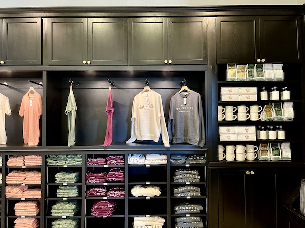 T-shirts on hangers and display of coffee mugs and bags of coffee at Magnolia Table Waco Texas