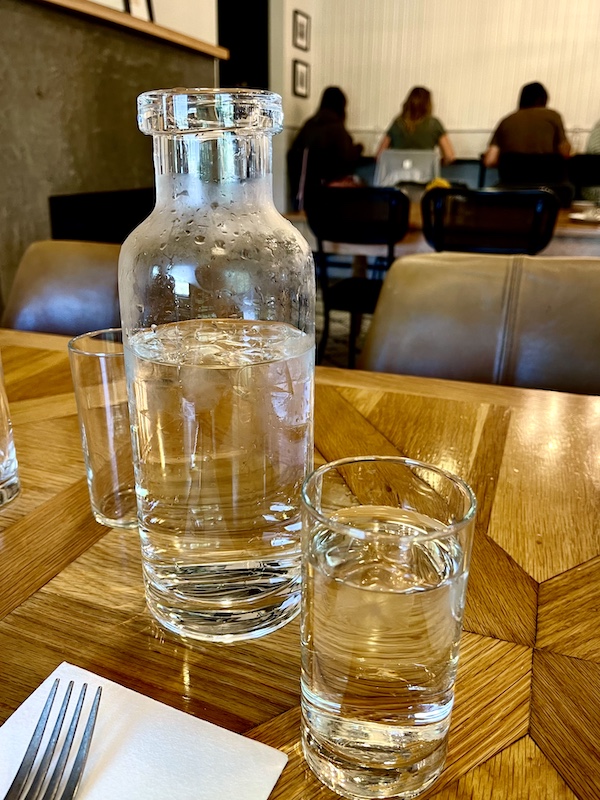 Upscale water bottle with glass stopper and water glasses on wood table at Magnolia Table Waco Texas