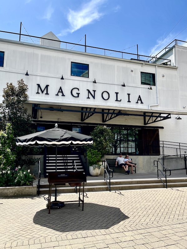 White building with black lettering Magnolia and black and white patio umbrella in front for shade at The Silos Waco Texas