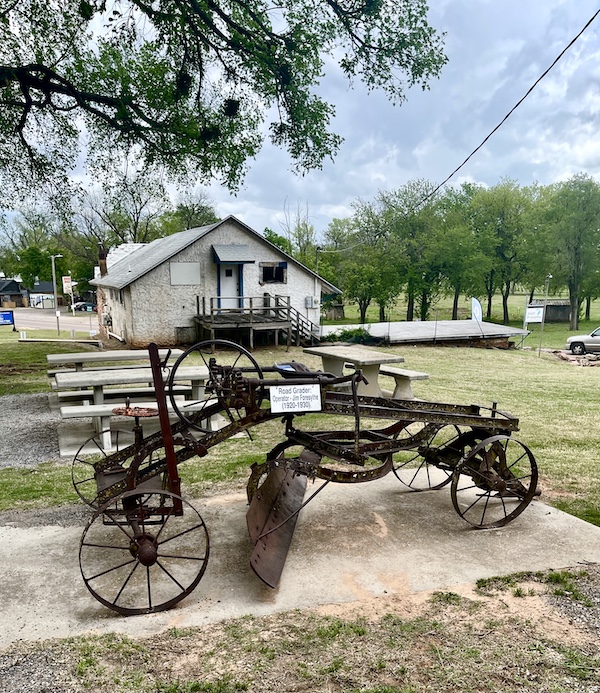 Antique road grader on display in foreground and small gray house in background at Arcadia Round Barn Oklahoma