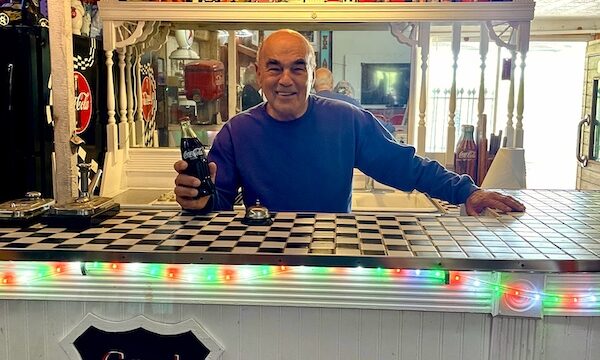 Steve behind the counter at a diner offering a bottle of Coke at John's Place Arcadia Oklahoma