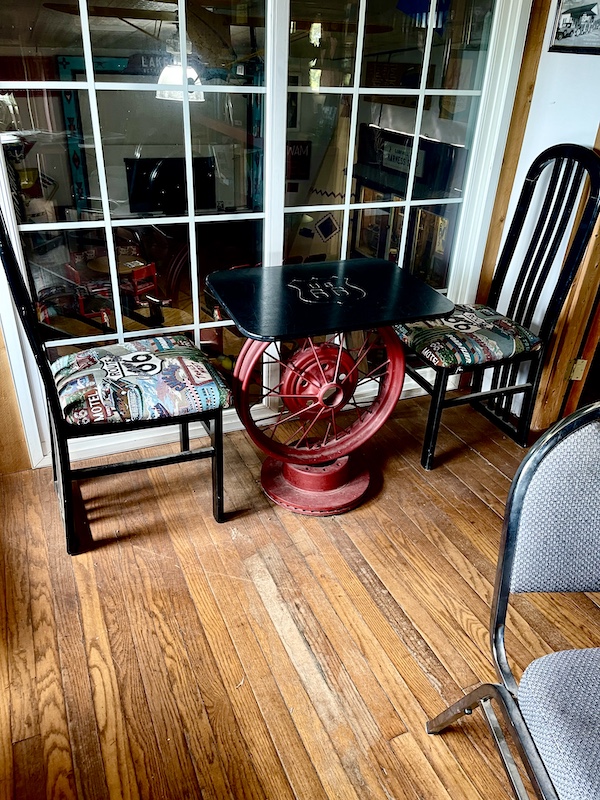 Red fire hose wheel is base of table and pair of chairs are upholstered with Route 66 fabric at John's Place Arcadia Oklahoma