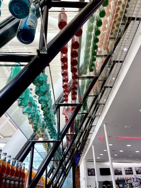 Slanted glass wall lined with shelfs an a rainbow of colored soda bottles at Pops Route 66 Arcadia Oklahoma