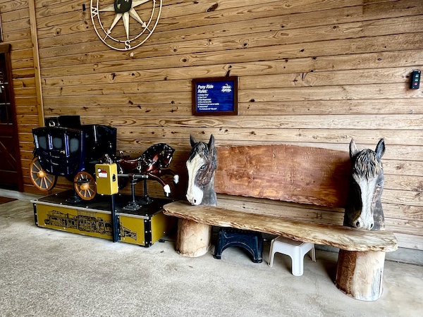 Wood bench with wood carved horse heads for arms sit next to a carriage with horses at Express Clydesdales Yukon Oklahoma